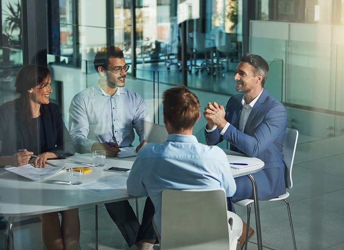 Insurance Solutions - Group of Business Professionals Sitting Around a Table Inside a Modern Office During a Conference Meeting